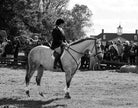 A person riding a grey horse in an outdoor setting, with spectators watching the event.