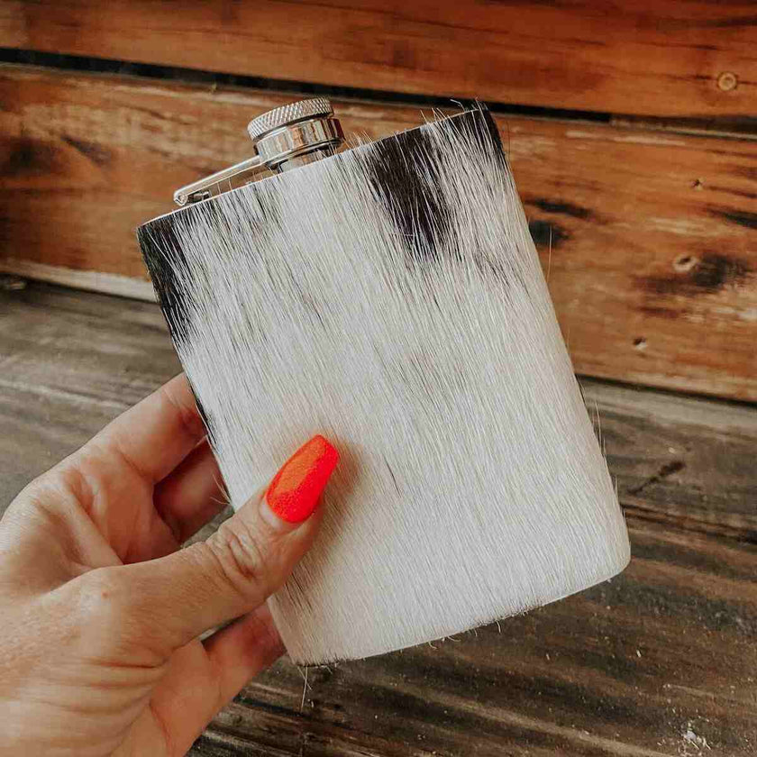 Person holding a white Cowhide Flask, Stainless Steel, against a wooden background