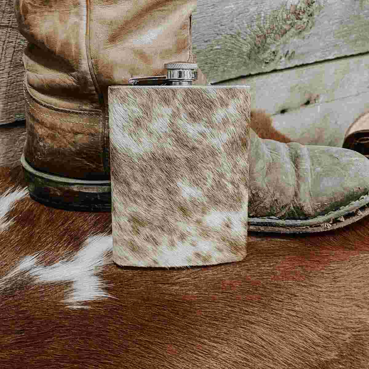 Flask with cowhide cover on a rustic wooden surface with cowboy boots in the background