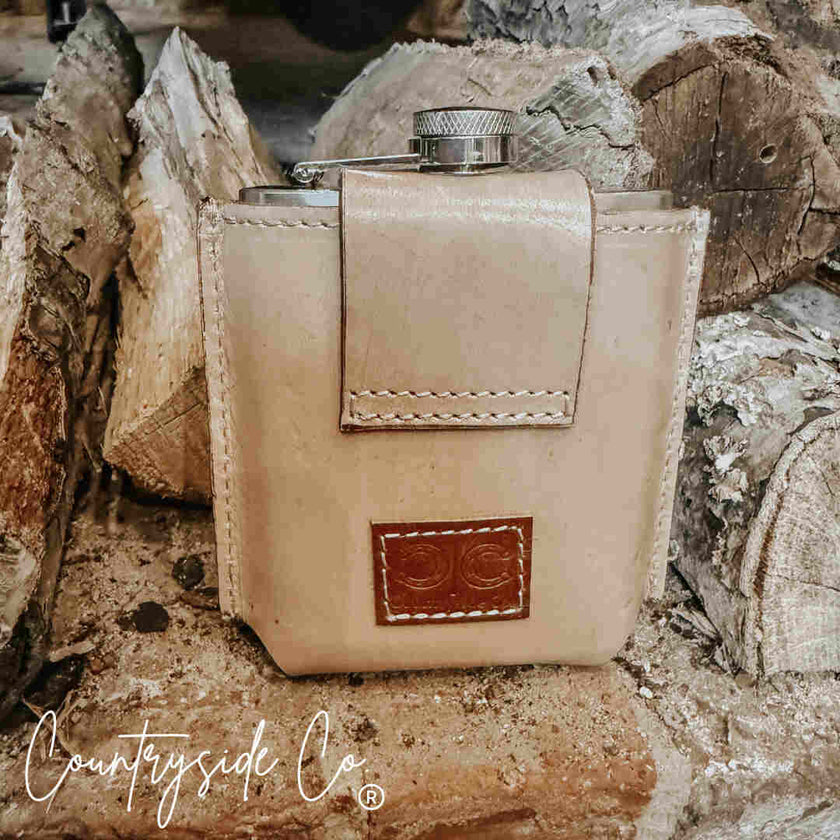 Desperado Tooled  Leather Flask with beige leather on wooden background with 'Countryside Co' branding.