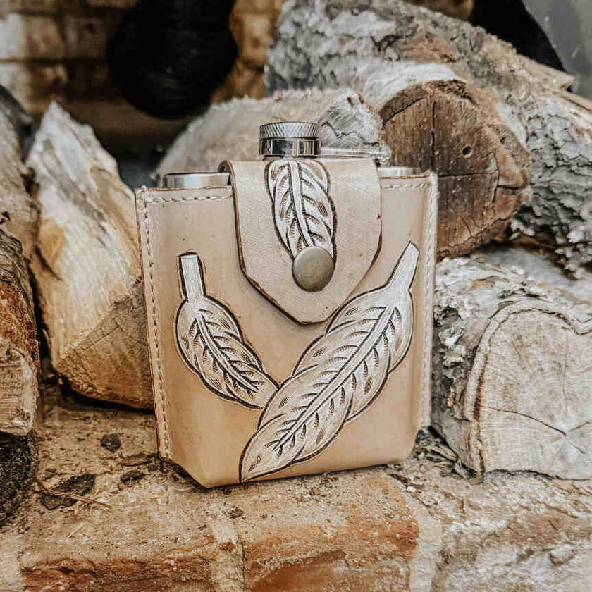 Desperado Tooled  Leather Flask with leather cover featuring feather designs on a wooden background