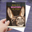 Hand holding a Donkey Birthday Card: Braying Good Birthday with a donkey's face and humorous text.