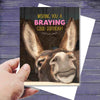 Hand holding a Donkey Birthday Card: Braying Good Birthday with a donkey's face and humorous text.