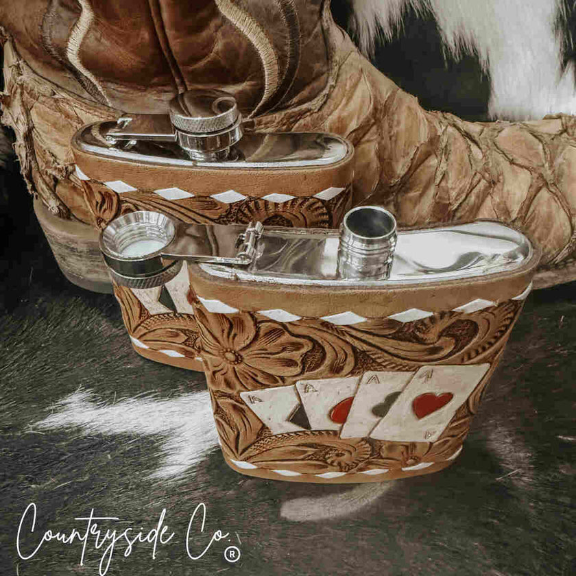 Decorative Leather Flask Stainless Steel with intricate designs and playing card symbols, placed on a textured surface.