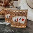 Two leather-bound Leather Flask Stainless Steel with embossed designs and playing card artwork on a wooden surface.