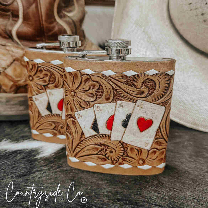 Two leather-bound Leather Flask Stainless Steel with embossed designs and playing card artwork on a wooden surface.