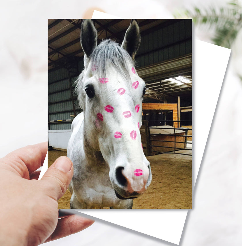 Horse Birthday Card: Horse Kiss Horse with pink kisses on a card held by a hand in a stable setting