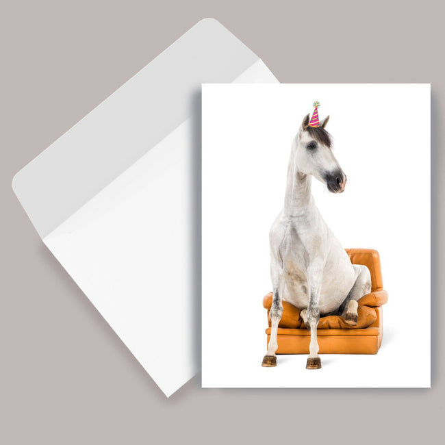 Horse Birthday Card: Horse Sitting with a horse on a couch and a birthday hat, next to an envelope on a gray background