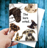 Horse Birthday Card: The Barn Voted with animals and text 'The barn voted...' held by a hand on a blue wooden background