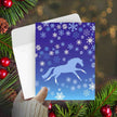 Horse Christmas Card - Galloping -with horse design on a blue background with snowflakes, surrounded by festive elements.