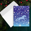 Horse Christmas Card - Galloping - with a blue horse design and snowflakes on a blue background, placed on a white envelope with a Christmas tree in the background.