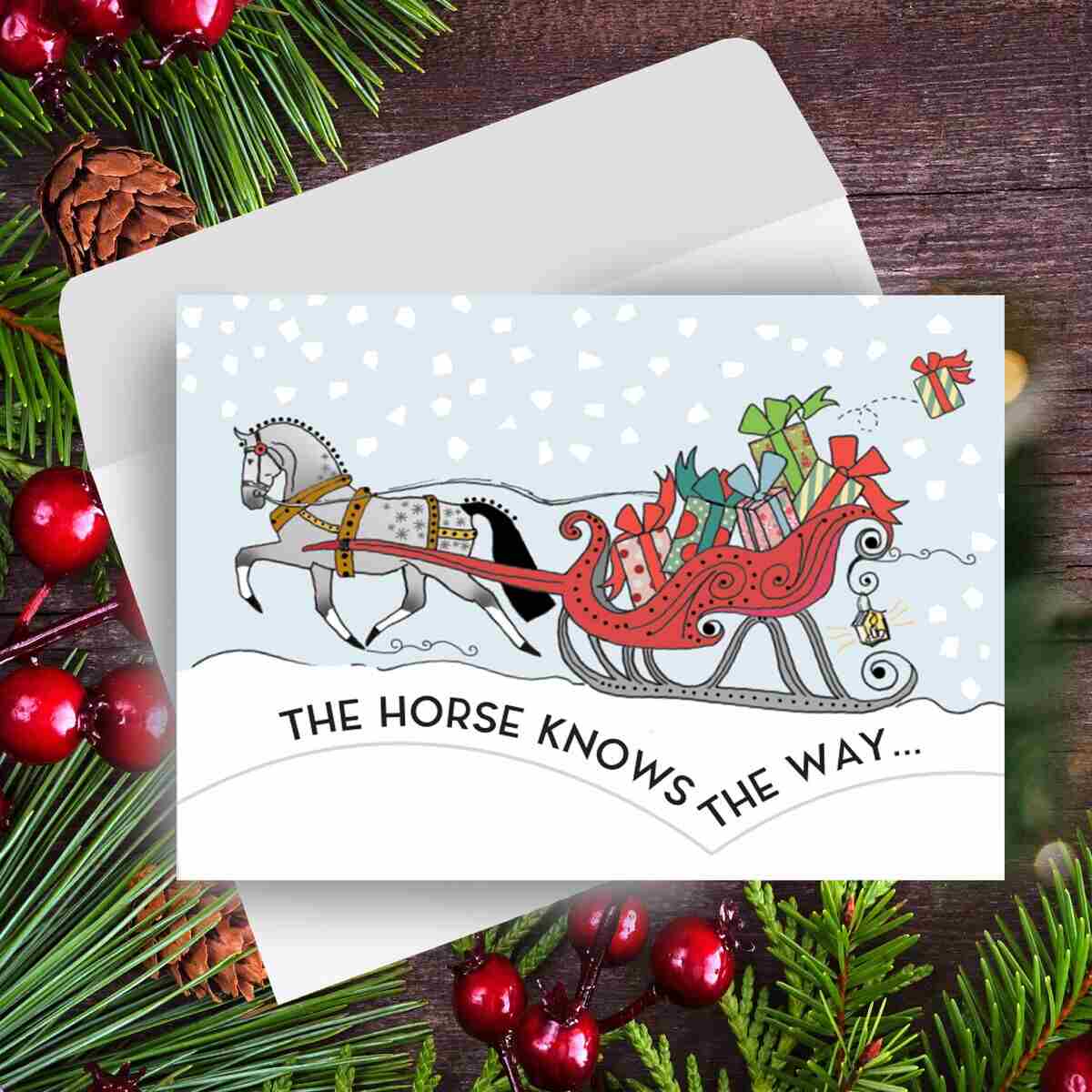 Horse Christmas Card - Santa Knows - with horse and sleigh illustration surrounded by festive decorations on a wooden surface.