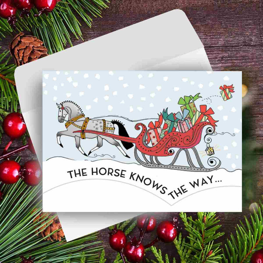 Horse Christmas Card - Santa Knows - with horse and sleigh illustration surrounded by festive decorations on a wooden surface.
