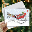Horse Christmas Card - Santa Knows - Hand holding a Christmas card with a horse and sleigh illustration against a blurred Christmas tree background.