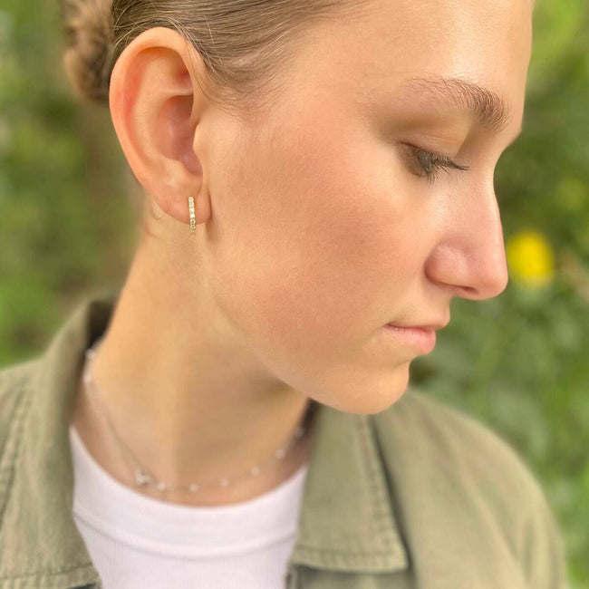 Horseshoe Hinge Earrings CZ Stones - Close-up of a person wearing earrings with a blurred green background