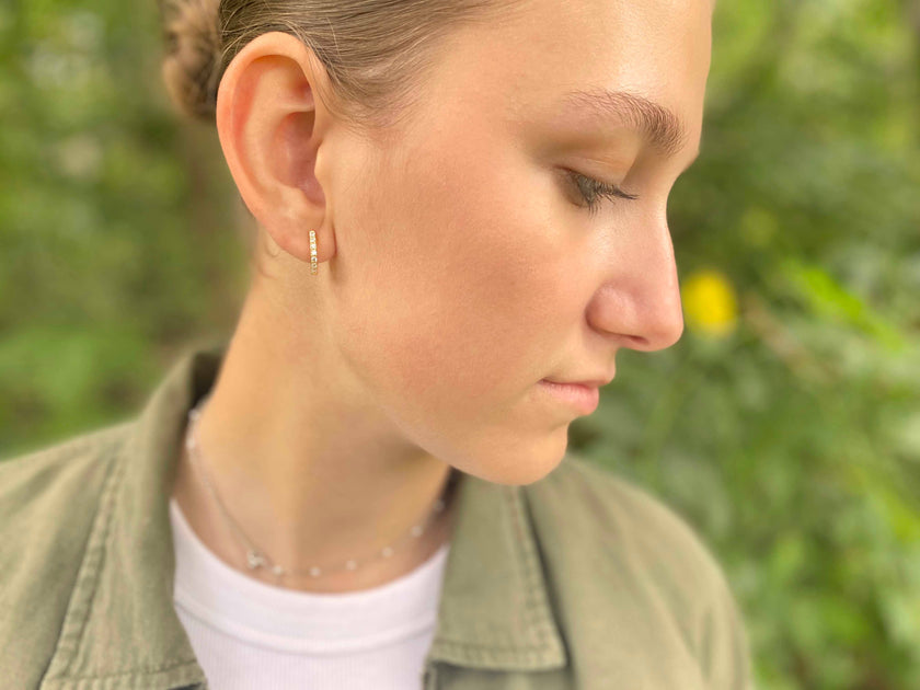 Horseshoe Hinge Earrings CZ Stones - Close-up of a person wearing earrings with a blurred green background