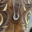 Silver horseshoe necklace on a brown boot leather background.