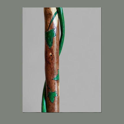 Wooden walking stick with green leaf designs on a gray background