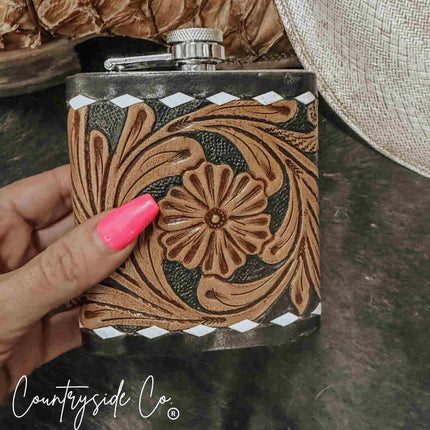 Hand holding a Leather Flask Stainless Steel with intricate brown designs on a dark surface, featuring 'Countryside Co' branding.