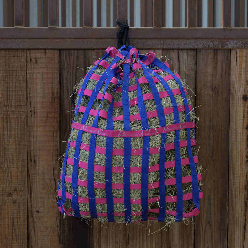 Professional's Choice Scratch-less Web Slow Feeder Hay Bag in raspberry color hanging on a stall.