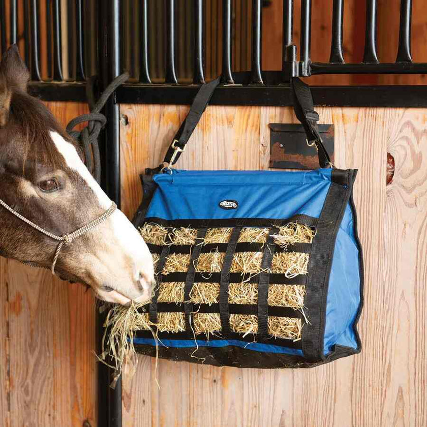Horse eating from a Hurricane blue Weaver Slow Feed Hay Bag attached to a wooden stable door.