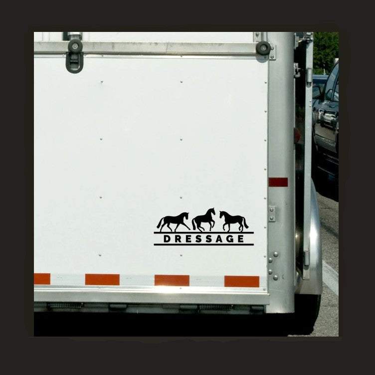 A vinyl decal with the word 'DRESSAGE' and silhouettes of horses above the text, placed on the side of a white horse trailer.
