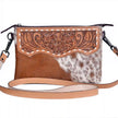 Brown cowhide crossbody bag with floral tooling and cowhide pattern on a white background